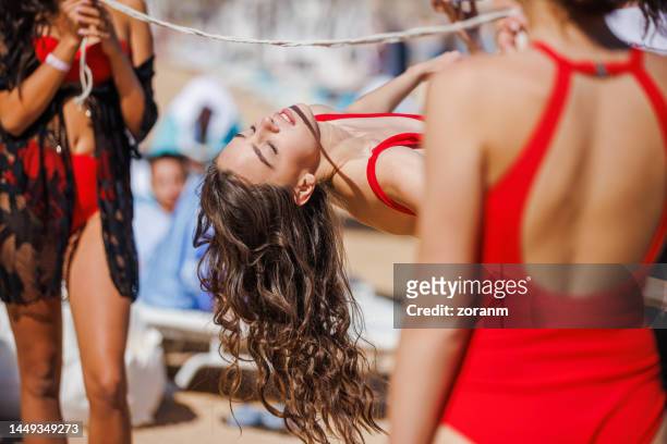 mujer joven en traje de baño inclinada hacia atrás y deslizándose bajo la cuerda del limbo en la playa - limbo blanco fotografías e imágenes de stock
