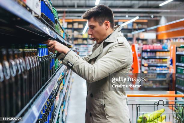 junger mann, der ein bier wählt, um es im supermarkt zu kaufen - buying beer stock-fotos und bilder