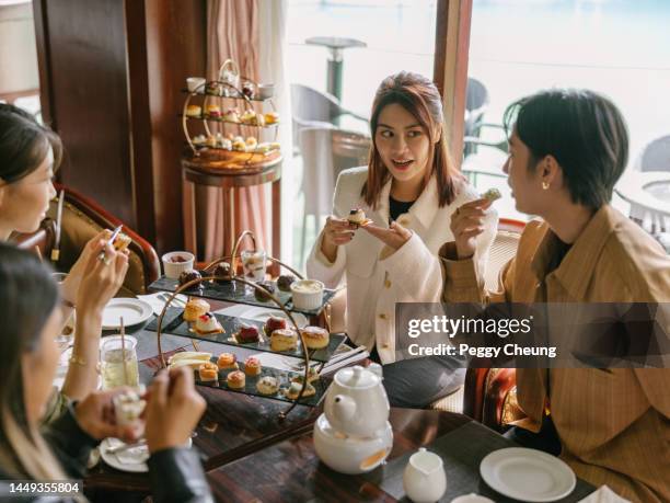 young happy asian women female friends eating cakes and dessert for afternoon tea in luxurious hotel or cafe indoors in daytime - tea time stockfoto's en -beelden