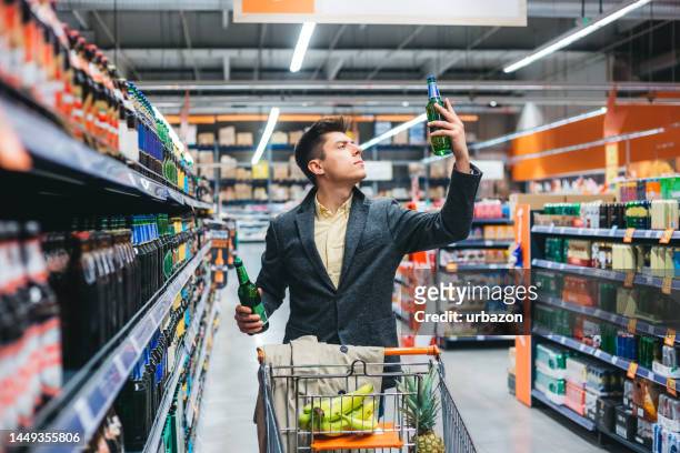 un jeune homme choisit une bière à acheter à l’épicerie - beer cart photos et images de collection