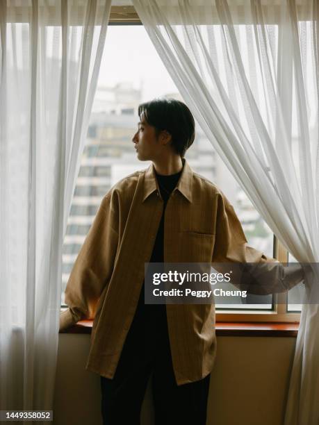 young stylish asian woman with short hair looking out the window and standing between curtains in hotel room indoors - manly room stock pictures, royalty-free photos & images