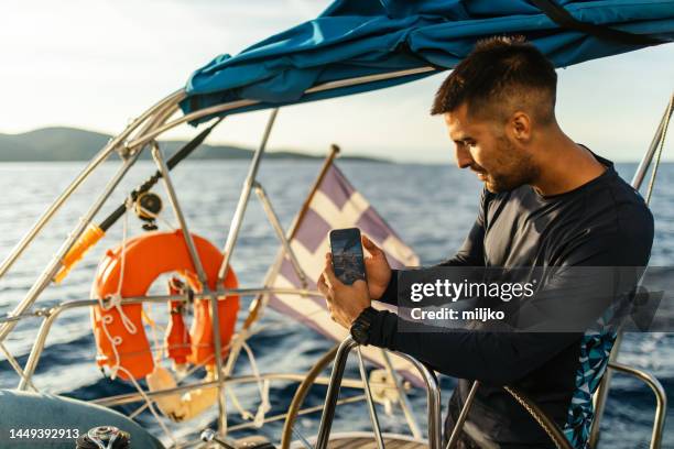 young man sailing alone in autumn and taking photo with mobile phone - boat captain stockfoto's en -beelden
