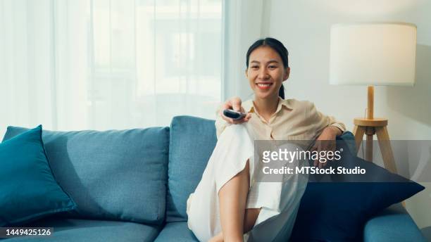 beautiful asian young woman on sofa click remote controller change channel on television choose favorite comedy or sitcoms in streaming online vod, video on demand at home. - cat holding sign imagens e fotografias de stock