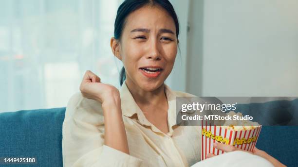 close-up young asian curious girl on sofa eat popcorn excited watch documentaries channel movie or mysteries show on television in streaming online vod, at home. - scandal television show stock pictures, royalty-free photos & images