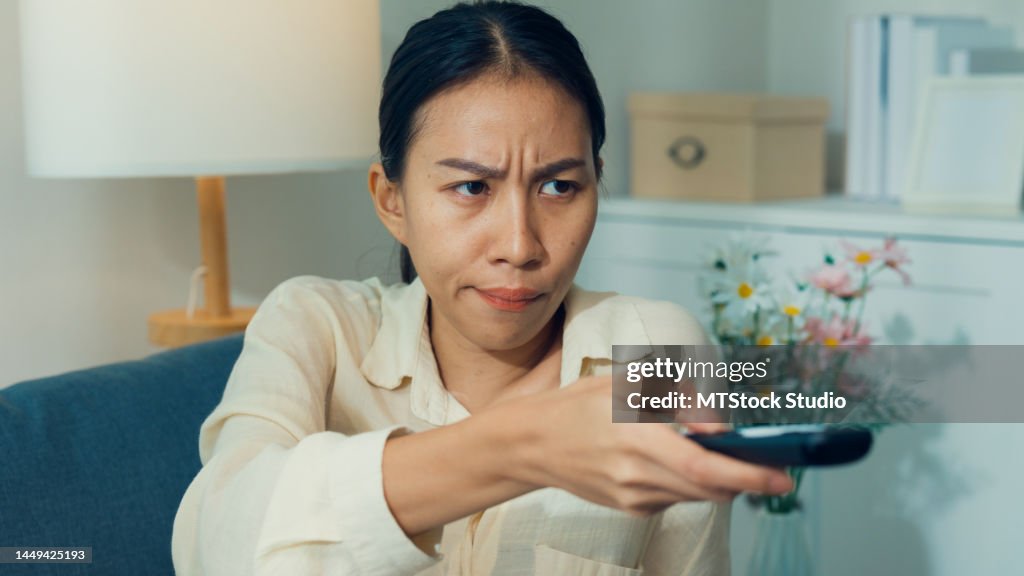 Jovem asia entediada mulher no sofá clique controlador remoto mudar desinteresse filme do canal ou show na televisão em streaming de VOD on-line, vídeo sob demanda em casa.