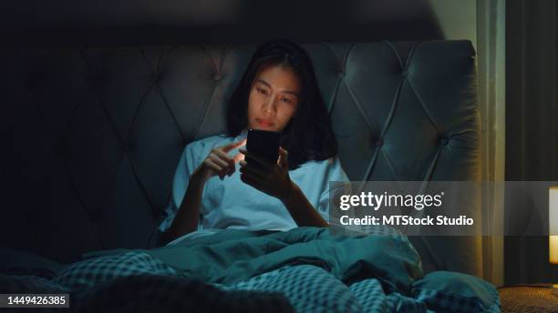 jeune asie fille dépendance aux médias sur le lit ne peut pas dormir diapositive écran de téléphone portable désintérêt ennuyeux avec le contenu social mobile à la maison la nuit. - relation à distance photos et images de collection