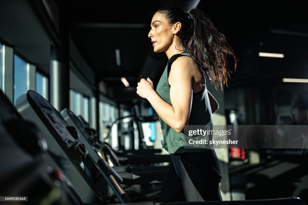 Entschlossene athletische Frau läuft auf Laufband in einem Fitness-Studio.