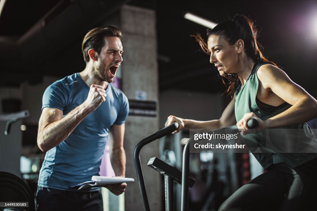Coach cheering for athletic woman on stationary bike in a gym.