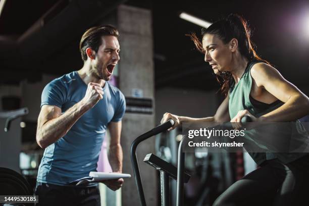 coach cheering for athletic woman on stationary bike in a gym. - spin instructor stock pictures, royalty-free photos & images