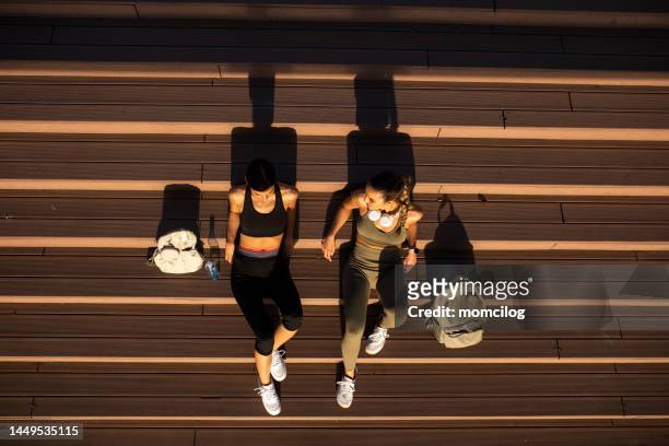 zwei befreundete athletinnen sitzen auf den stufen und ruhen sich vom laufen aus - frühjahrsmüdigkeit frau stock-fotos und bilder