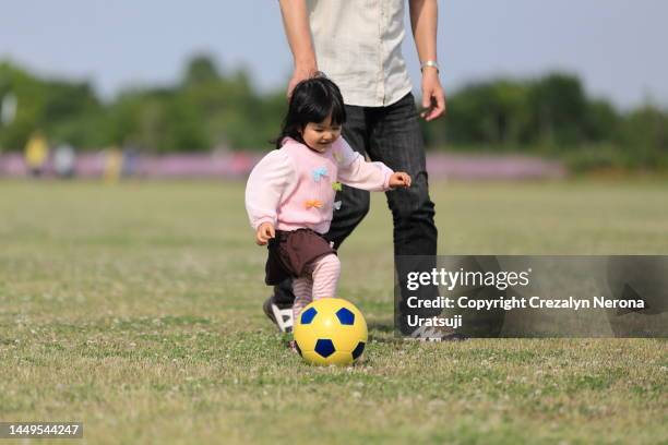 child learning how to play soccer at the public park with her father - baby kicking stock pictures, royalty-free photos & images