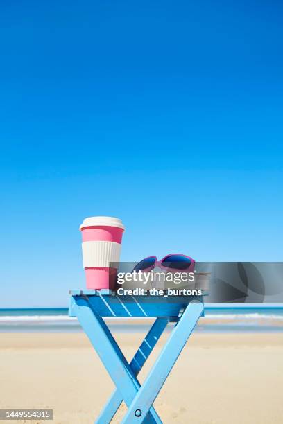 coffee cup, sunglasses and book on a table at beach and sea against sky - coffee table reading mug stock pictures, royalty-free photos & images