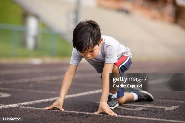 little boy in a sprint position on the track field - kids track and field stock pictures, royalty-free photos & images