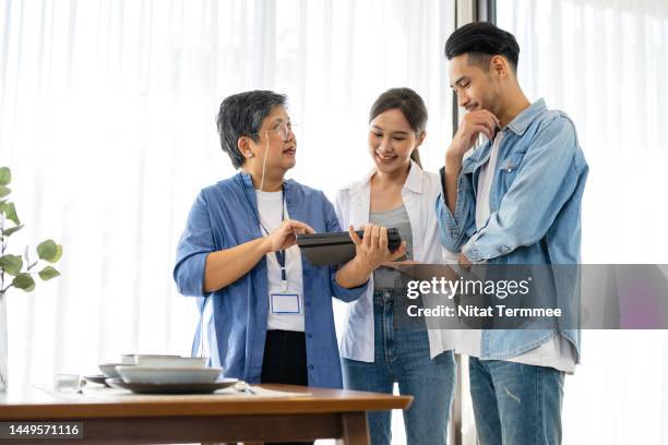 financial strategies of estate planning for family. a senior asian female real estate broker is showing a budget on a tablet computer and a decision with a couple to a home estate loan and promotion. - family decisions stock pictures, royalty-free photos & images