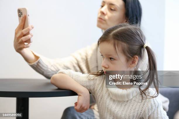 5 years old girl looks dissatisfied and unhappy about her mother using phone and ignoring daughter - ignoring stock pictures, royalty-free photos & images