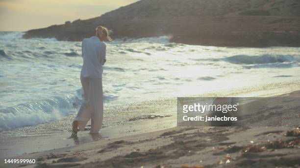 woman walking alone on a beach. looking off into distant sea enjoying the sand under her feet - i miss you stock pictures, royalty-free photos & images