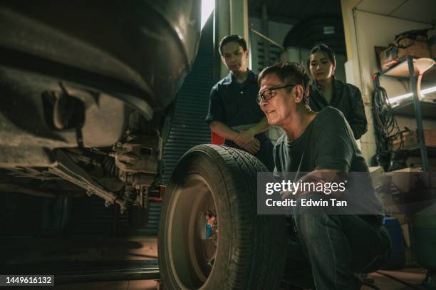 asian chinese senior mechanic showing teaching coworker apprentice changing tyre in workshop - training wheels stock pictures, royalty-free photos & images