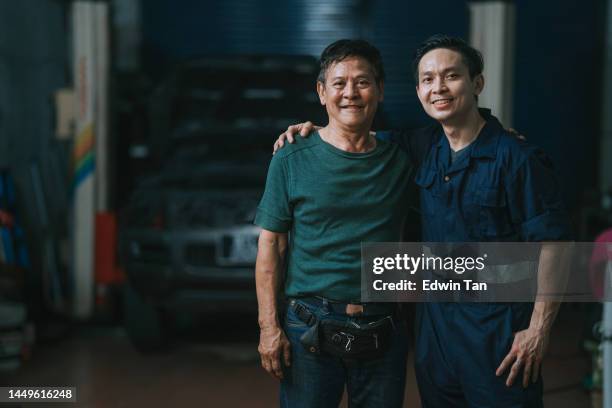 portrait 2 asian chinese mechanic looking at camera smiling standing in front of auto repair shop - malaysia father and son stockfoto's en -beelden