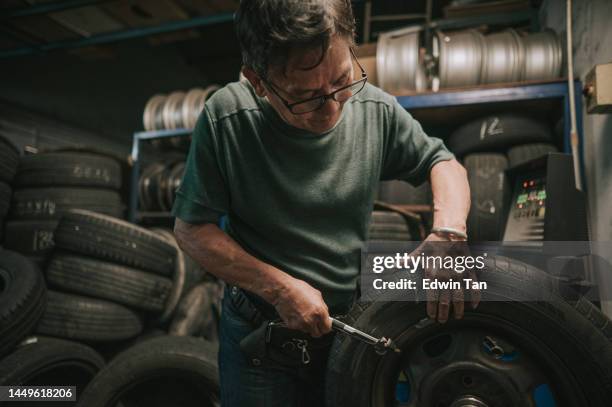 アジア系中国人の上級男性整備士が、自動車修理工場でタイヤを修理する機械とのバランスをとる - wheel rim ストックフォトと画像