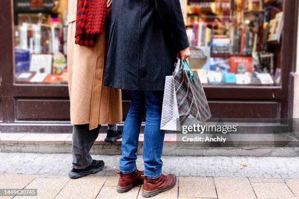 young couple with shopping bags looking at window display - shopaholic stock pictures, royalty-free photos & images