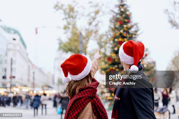 junge frau zeigt auf weihnachtsbaum - nikolausmütze stock-fotos und bilder