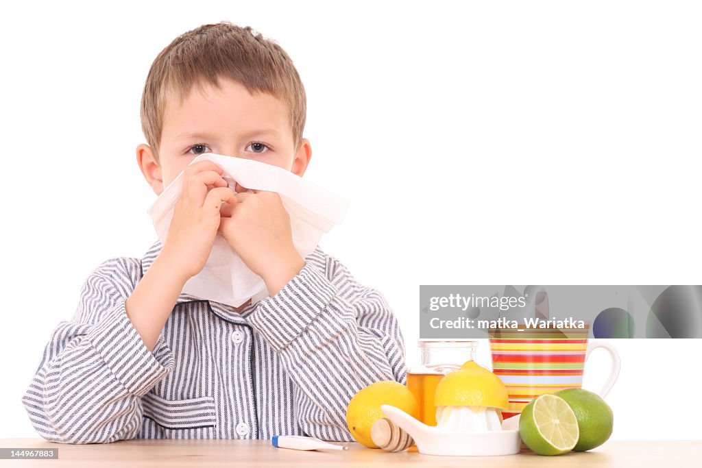 Young boy surrounded by citrus and tea blowing his nose