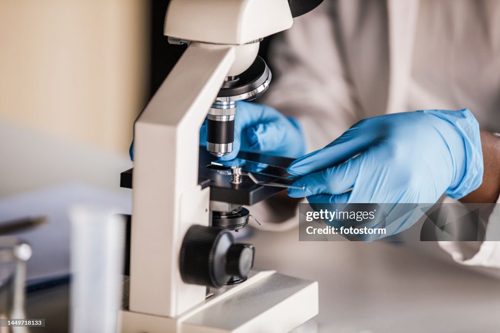 Lab tech in protective gloves putting a slide with a scientific sample under a microscope