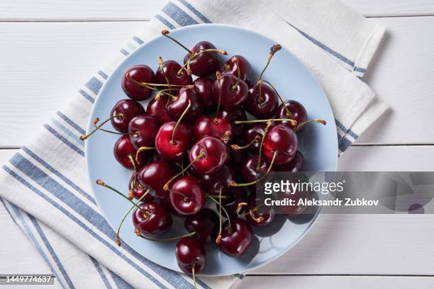 red ripe  sweet cherry on a plate, on the dining room or kitchen table. vegetarian, vegan and raw food food and diet. the concept of vegetarianism, veganism and raw food. vegetable food. from the farm to the table. ethical consumption. - cherry stock pictures, royalty-free photos & images
