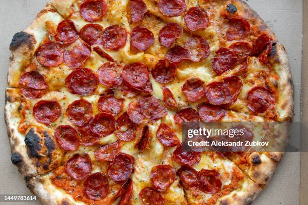 delicious italian pizza in a pizza box and a delivery box, on the table in a pizzeria. sliced pizza slice with tomatoes, pepperoni sausage and cheese. the concept of unhealthy lifestyle, overeating, junk food, fast food. delivery to your home or work. - pizza-de-pepperoni imagens e fotografias de stock