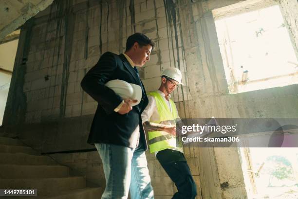 adult proprietor inspecting building under construction with the engineer on the construction site - capataz fotografías e imágenes de stock