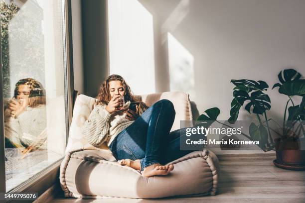 cheerful young woman enjoying tea and using smartphone in the morning. - hygge foto e immagini stock
