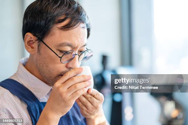 streamlining quality control in your coffee roastery. a male japanese barista tasting and smelling a cup of coffee at a coffee shop to control the quality of a coffee. - chef smelling food stock-fotos und bilder