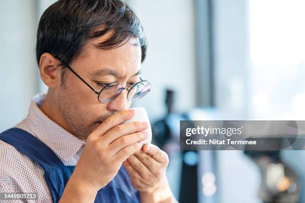 streamlining quality control in your coffee roastery. a male japanese barista tasting and smelling a cup of coffee at a coffee shop to control the quality of a coffee. - taste test stock pictures, royalty-free photos & images