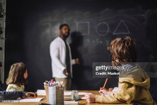 side view of boy looking at teacher teaching in classroom - kid blackboard stock pictures, royalty-free photos & images