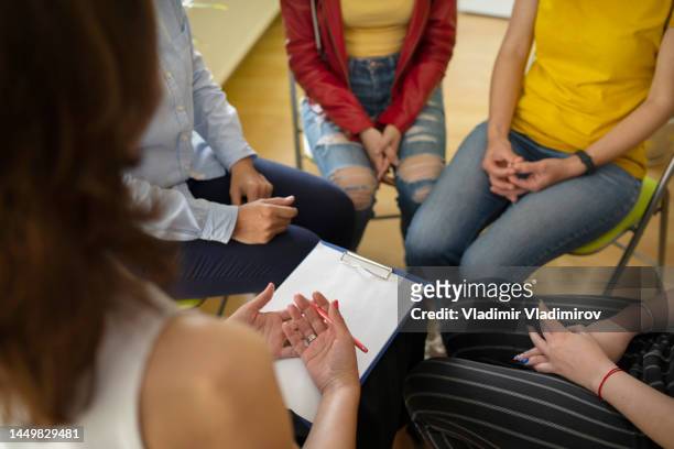 a female psychotherapist inquiring about symptoms occurring within mind from patients with mental health problems. group psychotherapy support concept - story telling in the workplace stock pictures, royalty-free photos & images
