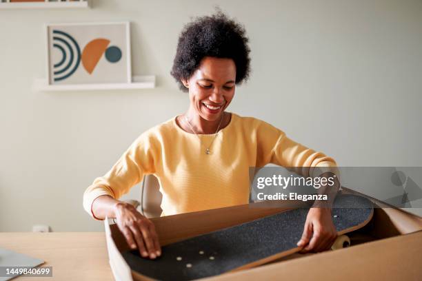 mid adult black woman shopaholic customer sitting and unpack parcel - skateboard shop stock pictures, royalty-free photos & images