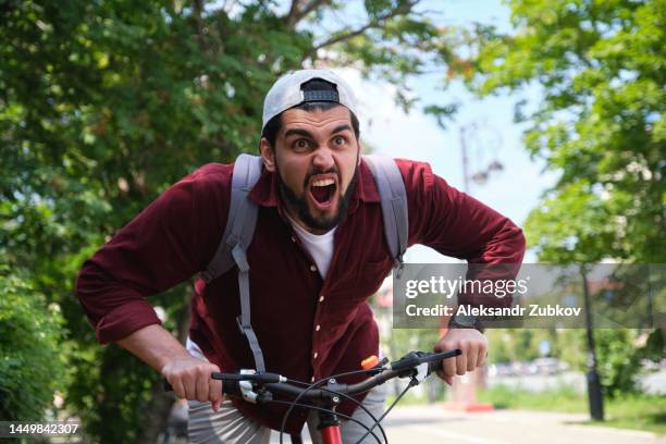 a young indian, a dark-skinned indian student, rides a bicycle down the street, in a public park along a bicycle path, against a background of green trees and shrubs. the concept of a healthy lifestyle, extreme sports, outdoor activities, adrenaline. - adrenaline park stock pictures, royalty-free photos & images