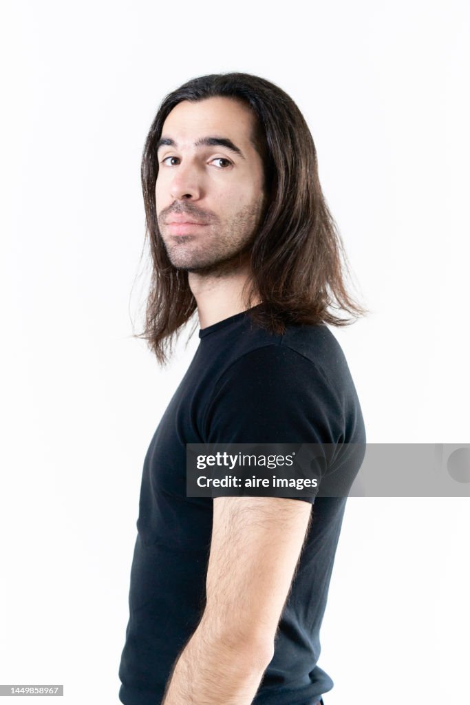 Adult male with long hair, turning around and looking at the camera while posing in a studio with white background.