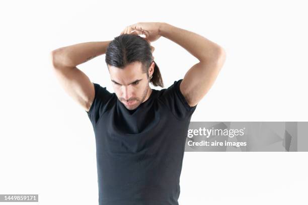 man in black t-shirt, looking down while fixing his long hair in a studio with white background. - man combing hair stock pictures, royalty-free photos & images