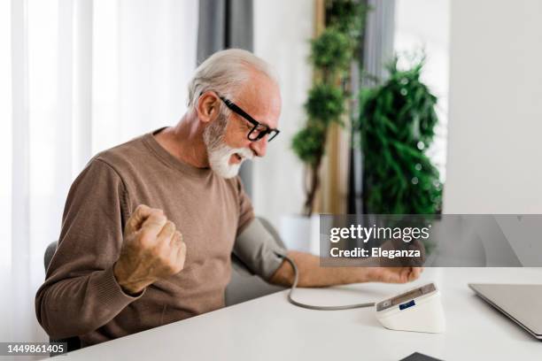 man sitting checking blood pressure at home - pressure gauge stock pictures, royalty-free photos & images