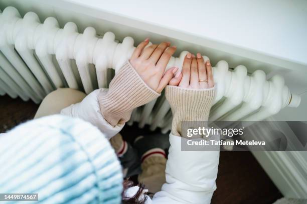 leaking of radiator. close up woman in hat getting warm with hands on heating radiator indoors - water heater stockfoto's en -beelden