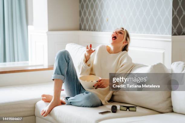tricks with popcorn, trying to catch. woman eating popcorn and watching tv at home - attraper photos et images de collection