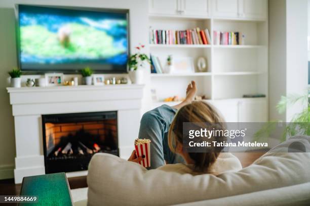 cozy hugge fireplace and watching tv. woman eating popcorn and watching tv on a big screen at home - chaîne de télévision photos et images de collection