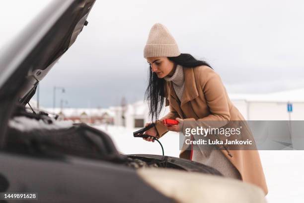 belle jeune femme essayant de démarrer sa voiture car la batterie est morte - auto batterie photos et images de collection
