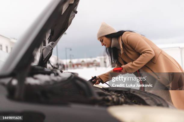 beautiful young woman trying to jump start her car since the battery is dead - cabos para arranque auxiliar imagens e fotografias de stock