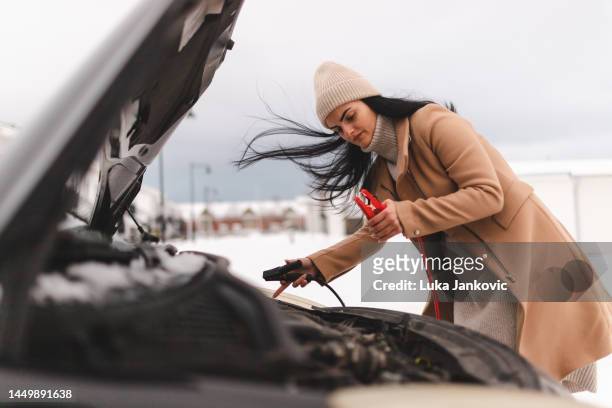 schöne junge frau, die versucht, ihr auto zu starten, da die batterie leer ist - winter panne auto stock-fotos und bilder