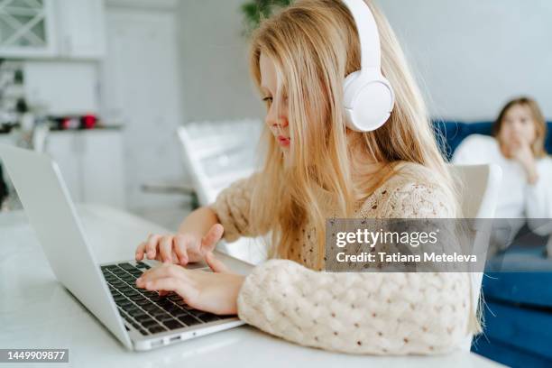 educational training course on the internet platform. little girl in headphones using her laptop at the desk in the kitchen - hands free apparaat stockfoto's en -beelden