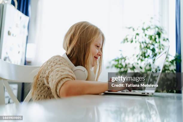 reading books online. electronic reader on a laptop. little girl in headphones on her neck using her laptop with black screen at the desk - hands free apparaat stockfoto's en -beelden