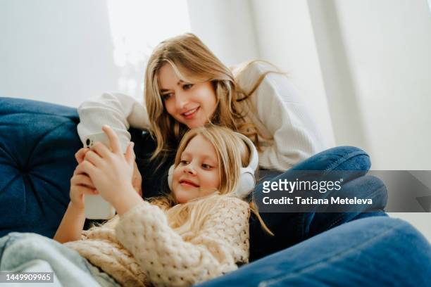 new mobile application for the family. smiling mother and daughter watching movies and listen to music together in living room - schumer holda news conf on deportation of parents of us citizen children stockfoto's en -beelden