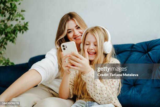 funny videos in social net, look at this. mother and daughter watching at smartphone screen and laughing on a sofa - schulkinder eltern stock-fotos und bilder